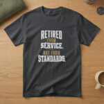 Black t-shirt with white and brass type, "Retired From Service. Not From Standards." on wood with a US flag
