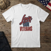 White t-shirt with red script and navy block type reading "Love Our Veterans", laid flat on wood with an American flag