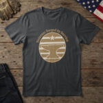 Black t-shirt with a brass badge of an anvil under a star and the words "Veteran: Forged by Service", on wood with a flag