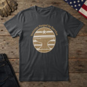 Black t-shirt with a brass badge of an anvil under a star and the words "Veteran: Forged by Service", on wood with a flag