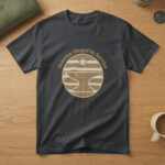 Black t-shirt with a brass badge of an anvil under a star and the words "Veteran: Forged by Service", on wood with a flag