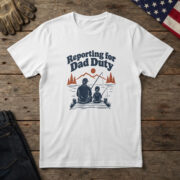 White t-shirt with line art of a dad and child fishing from a dock by pines and the words "Reporting for Dad Duty", on wood