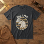 Black t-shirt with a bald eagle head in profile on a flag-stripe badge and the words "Est. 1776", on a pine workbench