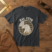 Black t-shirt with a bald eagle head in profile on a flag-stripe badge and the words "Est. 1776", on a pine workbench