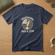 Navy t-shirt with a quill pen in an inkwell inside a flag badge and the words "Unalienable July 4, 1776", on a table