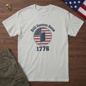 Ash t-shirt with an upright colonial pamphlet inside a flag badge and the words "Still Common Sense 1776", folded flag