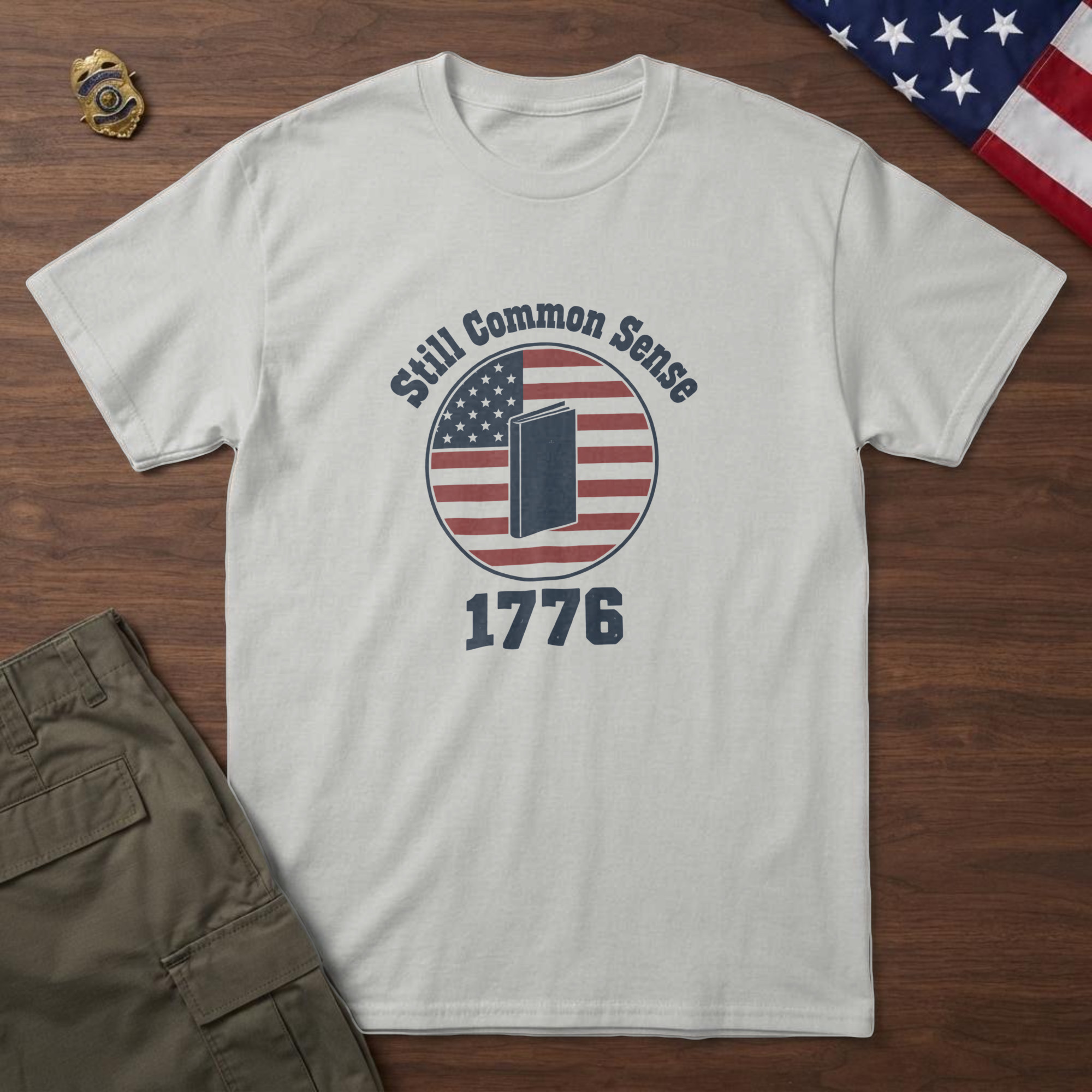 lfb-hero-15185 Ash t-shirt with an upright colonial pamphlet inside a flag badge and the words "Still Common Sense 1776", folded flag